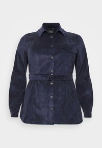 Mörkblå skjorta med knappar i mjukt tyg, som har långa ärmar, en bröstficka och ett bälte med ett runt spänne. Slät textur.