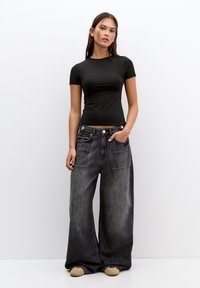 Black fitted t-shirt paired with loose, dark gray denim wide-leg jeans, featuring a button fly and side pockets, worn with beige shoes.