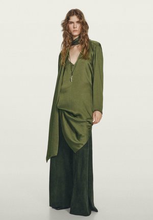 Green satin top with draped front, paired with wide-leg green trousers. Long sleeves and a neck scarf detail complete the ensemble.