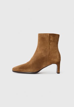 Stivaletto in camoscio marrone con punta affusolata e tacco medio sottile, vista laterale su sfondo bianco uniforme.