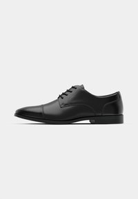 Zapato de vestir de cuero negro con punta redonda, textura suave, seis ojetes y una suela baja negra. Presenta una costura sutil a lo largo de la punta.