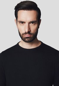 Czarny sweter z okrągłym dekoltem wykonany z gładkiego materiału dzianinowego, o dopasowanym kroju i ribbrowanym dekolcie na neutralnym szarym tle.