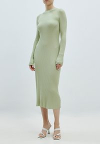 Robe côtelée vert menthe à manches longues et silhouette ajustée. Associée à des sandales à talons hauts argentées à brides. Texture lisse.