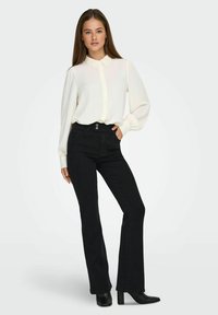 Blusa blanca de botones con tejido texturizado y cuello de encaje, combinada con jeans negros de campana y botas de tacón negras.
