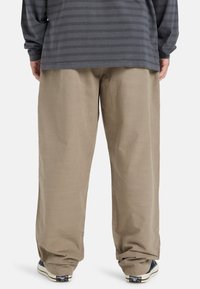 Beige wide-leg pants with a smooth texture, paired with dark gray striped long-sleeve shirt and black sneakers with white soles.