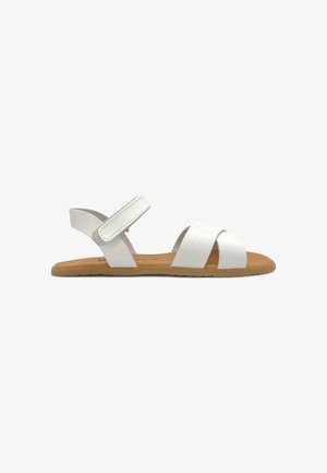 Hvid flad sandal med to forreste remme og en justerbar ankelrem på en tan-sål, vist fra siden på en hvid baggrund.
