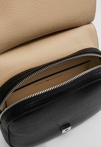 Black textured leather bag with a beige top flap, silver zipper, and a square metal accent. Inner lining features brand logo.