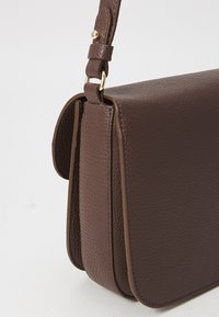Brown leather shoulder bag with a textured surface, structured design, gold hardware accents, and an adjustable strap.