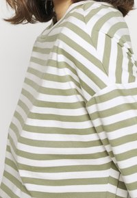 Grøn- og hvidstribet langærmet top med en afslappet pasform. Blødt stof, rund halsudskæring og sænkede skuldre.
