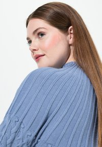 Ljusblått stickat tröja med ribbstruktur, med rund hals och intrikata fläta detaljer på ärmarna.