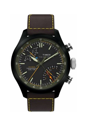 Chronografické hodinky Timex s černým ciferníkem, žlutými akcenty, tachymetrickou stupnicí, subciferníky pro dvojí čas a hnědým koženým páskem se žlutým prošíváním.