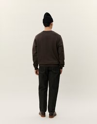 Felpa marrone scuro con colletto rotondo, abbinata a jeans di denim scuro. Un berretto nero completa il look. Vista posteriore, sfondo neutro.
