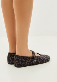 Black suede Mary Jane shoes with a leopard print pattern, featuring a side buckle strap and a flat sole.