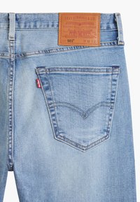 Poche arrière de jean Levi's bleu clair avec surpiqûre arcuate emblématique, étiquette rouge Levi's et patch en cuir marron indiquant la taille W32 L32.