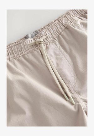 Shorts de bain beige clair avec une taille élastique, fermeture par cordon de serrage et texture lisse. Présente des coutures discrètes et une poche latérale.