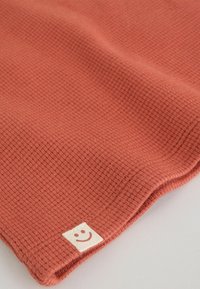 Tissu orange brûlé à texture douce avec une petite étiquette blanche présentant un simple visage souriant dans un coin.