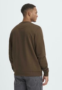 Bruine sweatshirts met lange mouwen, ronde hals en geribbelde manchetten. Stof lijkt zacht en textuur te hebben. Gemaakt in combinatie met grijze jeans.