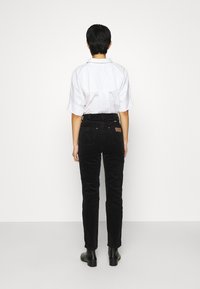 Černé kordové kalhoty s úzkým střihem, s polovičním pasem, zadními kapsami a koženou nášivkou v barvě tan. Spárované s bílou košilí s límečkem.