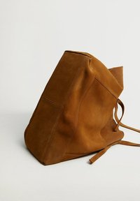 Brązowa zamszowa torebka w kształcie wiadra z szerokim dnem i luźną strukturą, z minimalistycznym przeszyciem i dwoma cienkimi ramiączkami na białym tle.
