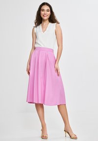Biała bezrękawnikowa bluzka z dekoltem w serek w połączeniu z różową spódnicą do kolan w plisy. Modelka nosi złote sandały na obcasie.