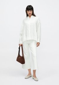 Λευκό λινό πουκάμισο με κουμπιά συνδυασμένο με λευκό παντελόνι με φαρδιά πόδια. Καφέ σουέντ τσάντα ώμου. Γκρι παπούτσια τύπου slip-on. Απλός, μινιμαλιστικός σχεδιασμός.