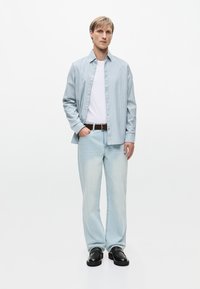 Ανοιχτό μπλε καρώ πουκάμισο πάνω από λευκό T-shirt, σε συνδυασμό με ανοιχτό μπλε τζιν και μαύρα παπούτσια. Διαθέτει κλασική γραμμή και ελάχιστες λεπτομέρειες.