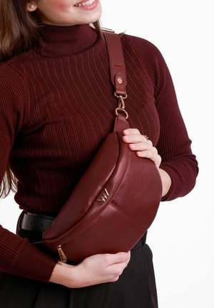 Burgundy leather crossbody bag with a curved design, adjustable strap, gold-tone hardware, and a smooth texture. Zipper detail visible.