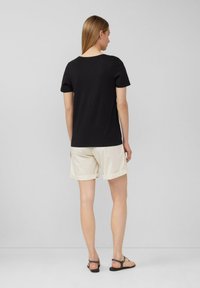 Schwarzes T-Shirt mit kurzen Ärmeln, kombiniert mit cremefarbenen Shorts. Das T-Shirt hat einen runden Halsausschnitt, und die Shorts haben umgeschlagene Säume.