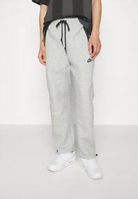 Ljust grå träningsbyxor i mjukt material med en avslappnad passform, med en svart Nike-logotyp och dragsko i midjan, stylade med vita sneakers.