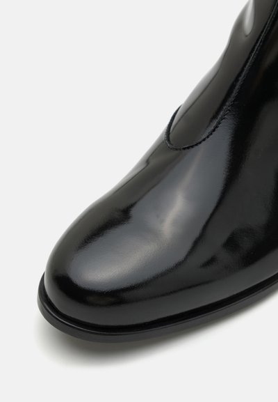 Crne lakirane gležnjače s okruglim vrhom, glatkom površinom, elastičnom bočnom pločom i suptilnom petom. Minimalistički dizajn i elegantan završetak.