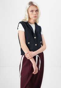 Marine gebreide vest met een cropped ontwerp, ingelegd kraag en twee voorzakken. Heeft goudkleurige knopen en een gestructureerde afwerking.