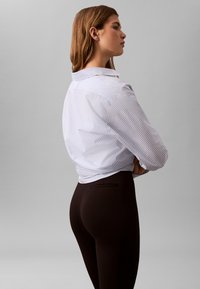 Hvit skjorte med blå striper, knappedown-krage, lange ermer og en avslappet passform; kombinert med høytlivs svarte leggings.