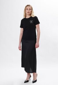 Sort t-shirt med korte ærmer og sommerfugleudsmykning. Sammen med en flagrende sort maxi-nederdel og sorte hælede sko med udsmykning.