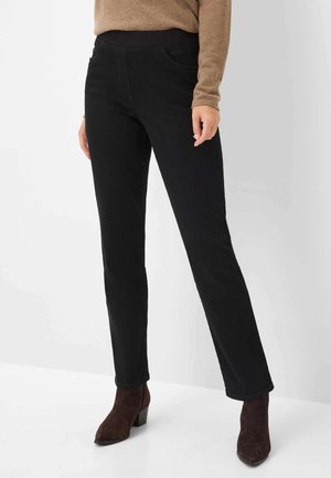 Zwarte jeans met een slim fit, voorzien van een soepele tailleband en zakdetails, gecombineerd met bruine enkellaarsjes, op een effen achtergrond.