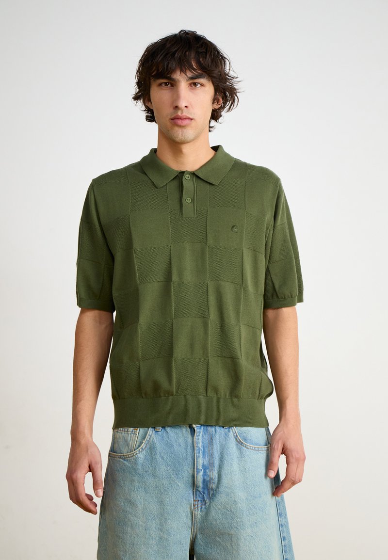 Grønn strikket polo med kort erm, med et teksturert rutemønster og ribbestrikket kant, kombinert med lyseblå denimshorts.