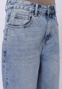 Jeans din denim albastru deschis cu talie înaltă, design cu cinci buzunare și textură ușor desprinsă. Cusătură în nuanță contrastantă de portocalie.