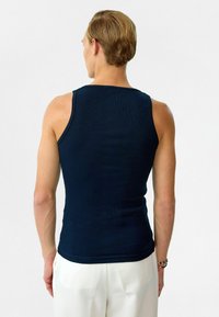 Navyblauwe geribbelde tanktop met een aansluitend ontwerp, mouwloos en met een ronde halslijn. Draag het met witte plooibroeken.