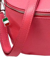 Ronde roze leren handtas met ritsluiting, met een gladde textuur en een zilveren charme die de Italiaanse vlag toont.