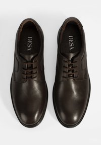 Braune Lederschuhe mit glatter Oberfläche, runden Zehen und Schnürdesign. Auffällige Nähten und eine gepolsterte Innensohle für zusätzlichen Komfort.