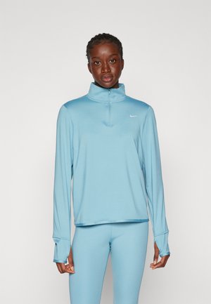 Himmelblaues Sportoberteil mit hohem Kragen und Reißverschluss, aus weichem Stoff gefertigt. Lange Ärmel haben Daumenlöcher. Kombiniert mit passender Leggings.