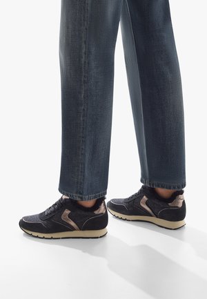 Sneakers neri con tessuto testurizzato, dettagli in suede e finiture dorate. Abbinati a pantaloni in denim scuro, leggermente larghi.