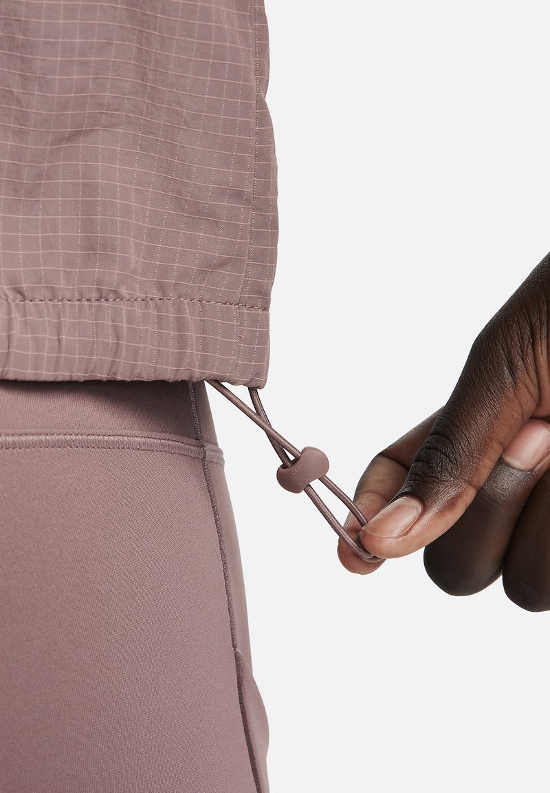 Lichte mauve jas met een geruit patroon, voorzien van een trekkoord aan de onderkant, verstelbaar met een plastic sluiting.