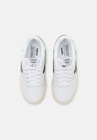 Hvite sneakers med perforerte detaljer, flate snørebånd, svarte aksenter på sidene og en gummisåle i kremfarge. Har Snoopy-grafikk på innsiden.