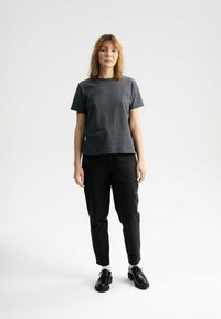 Graues kurzärmeliges T-Shirt, schwarze schmal geschnittene Hose, schwarze Schuhe mit dicken Sohlen. Minimalistisches Design mit lockerer Passform und einfarbigem Look.