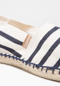 Canvas-Espadrilles mit navy- und weißen Streifen, ausgestattet mit einer geflochtenen Jutesohle und einem kleinen braunen Etikett an der Seite.