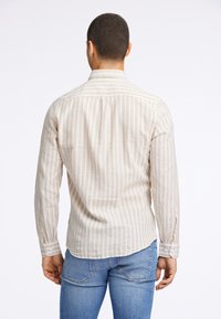 Camicia a maniche lunghe di un beige chiaro con righe verticali, polsini abbottonati e una yoke posteriore. Il tessuto appare liscio con una texture morbida.