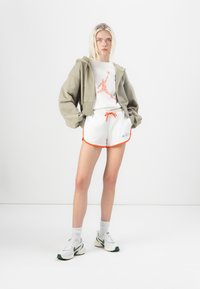 Conjunto de ropa deportiva para hombre que incluye una sudadera corta gris, una camiseta blanca con el logo de Jordan, pantalones cortos blancos con ribete naranja y zapatillas.