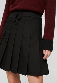 Jupe plissée noire avec une texture lisse, dotée d'un cordon de serrage noir à la taille, associée à un pull en maille bordeaux.