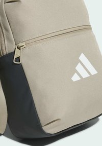 Béžový látkový batoh s tmavomodrým dnom, so zipsovou kapsou a bielym logom. Textúrovaný povrch s vystuženým šitím.