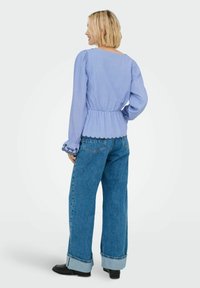 Blouse bleu à rayures avec des manches bouffantes et un ourlet en scallop, associée à un jean en denim taille haute et large avec des bottines noires.